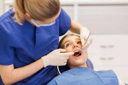 dentist with mirror checking girl teeth